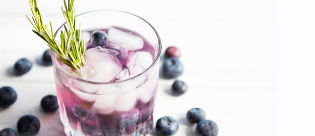 A purple drink in a glass with icecubes, blueberries and a sprig of rosemary